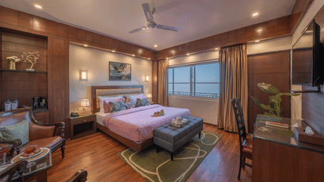 A bedroom at Perfectstayz Premium The Pride, Mussoorie, featuring a king size bed, a work area with table and chair, an armchair, side tables, and a window with scenic views.