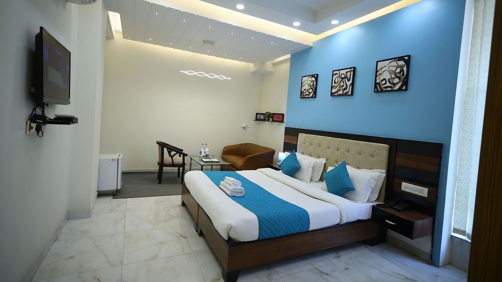 A room with two single beds featuring blue and white bedding, a television, and framed artwork on the wall - Asian Suites Cyber Park, Gurgaon