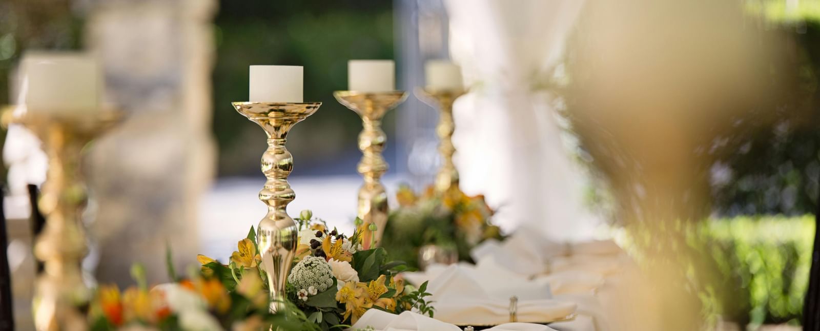 A long table covered with a table cloth decorated with shinny candle stands and well-arranged cutlery.
