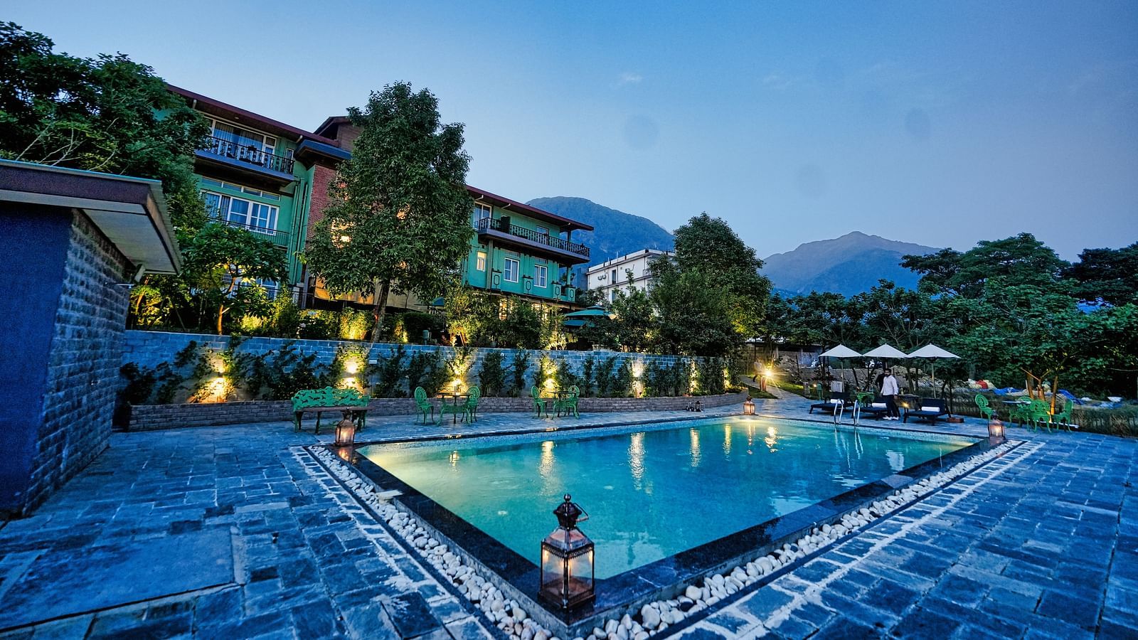A picture with luxurious swimming pool, beautifully lit around and a scenic mountain view in the background - Atman, Dharamshala