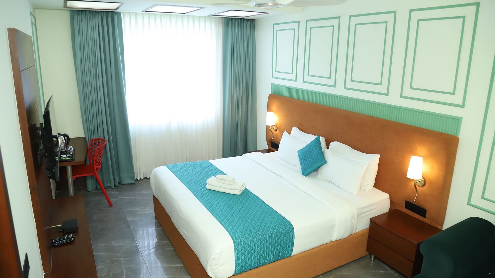 A comfortable room includes a double bed with a turquoise accent and wooden furniture - Asian Suites IFFCO Metro, Gurgaon