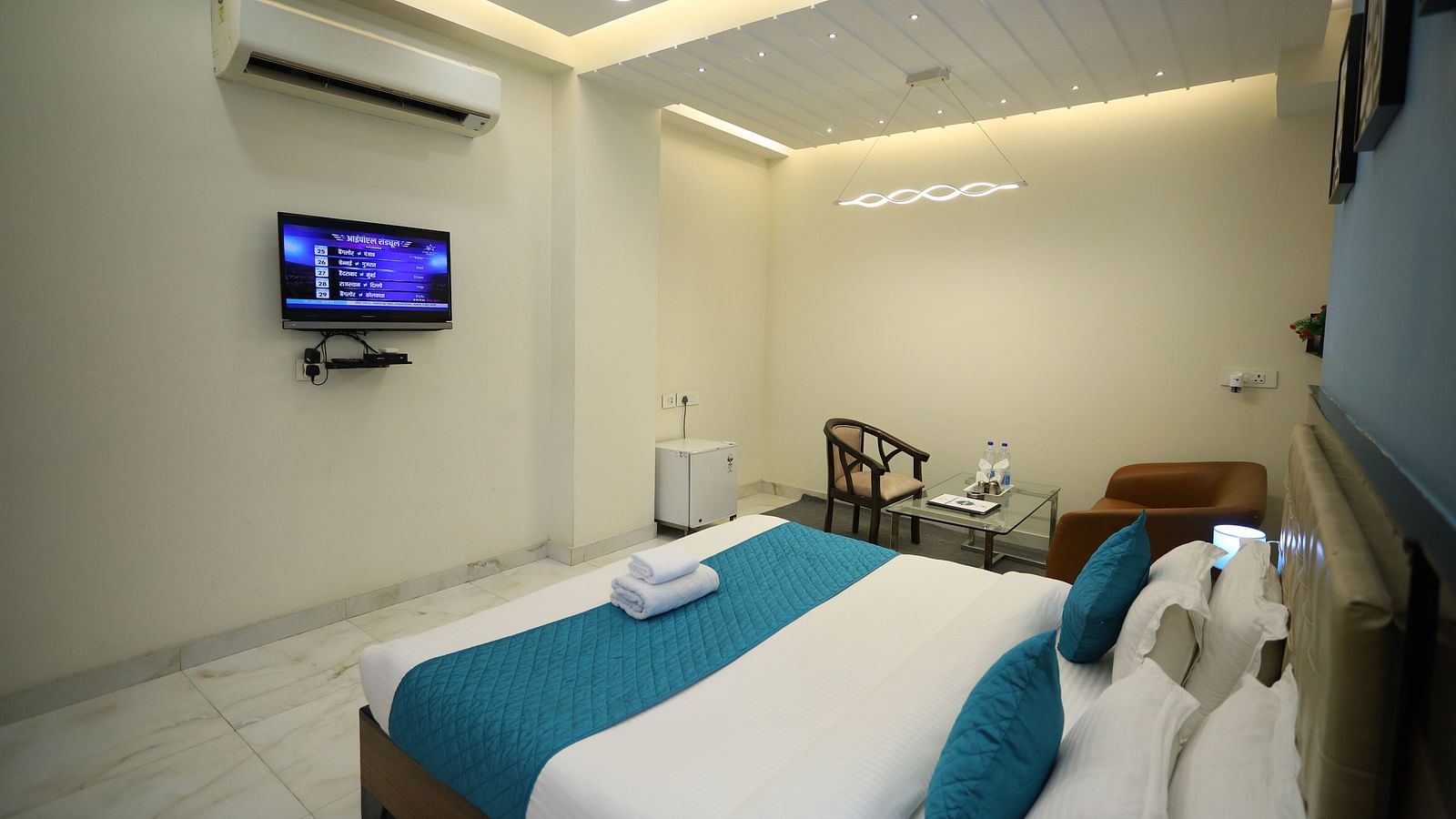 A room with a double bed, a television mounted on the wall, a chair, and modern lighting fixtures - Asian Suites Cyber Park, Gurgaon