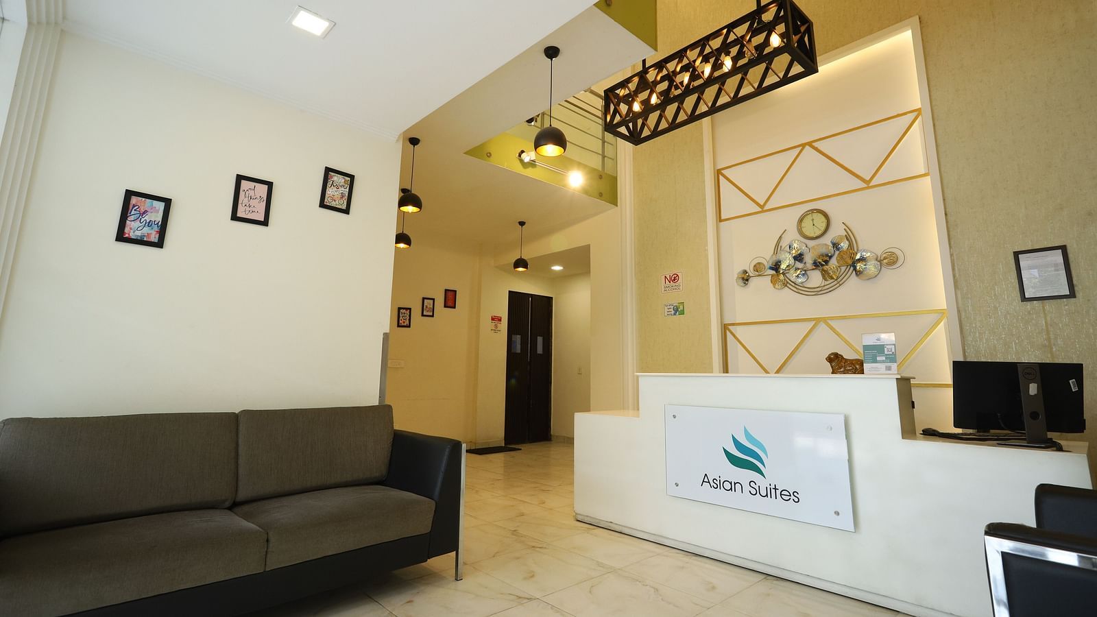 A reception area with a dark sofa and a white counter featuring a logo, illuminated by modern lighting fixtures - Asian Suites Cyber Park, Gurgaon