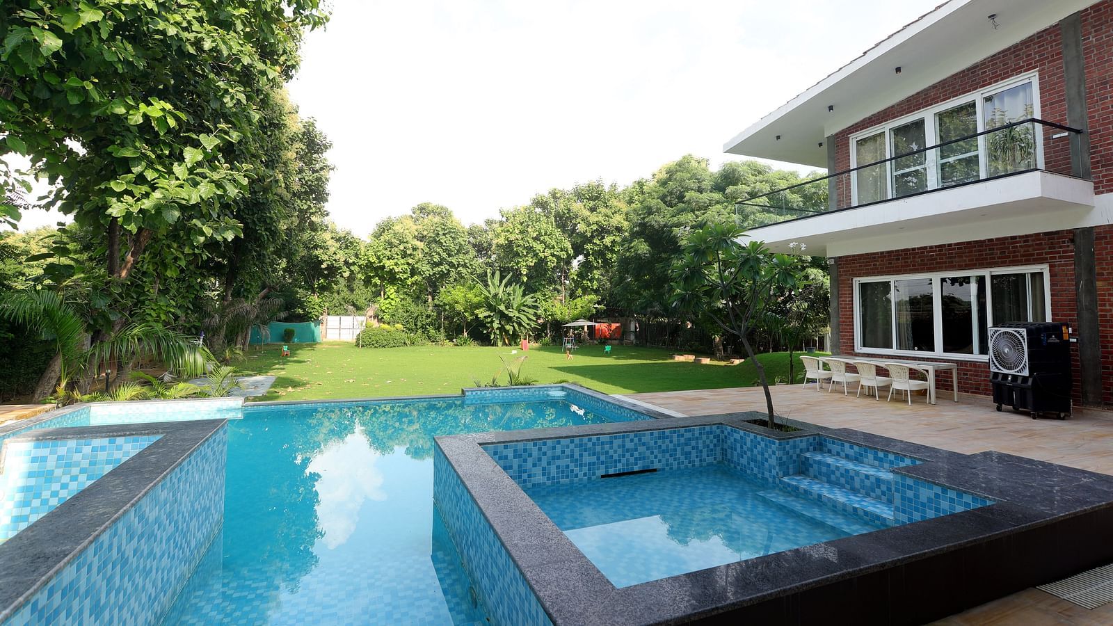 Spacious outdoor pool surrounded by greenery and modern villa exterior at Tisya Farms, Gurgaon.