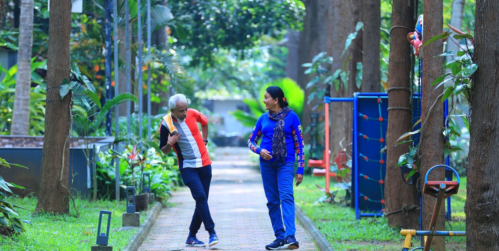 Image of a man and a woman walking on a footpath with trees and plants around them.