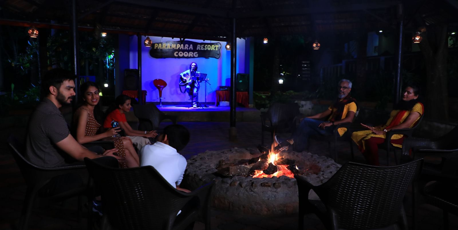 Image of a group of people sitting around a bonfire at Parampara Resort & Spa, Kushalnagar.