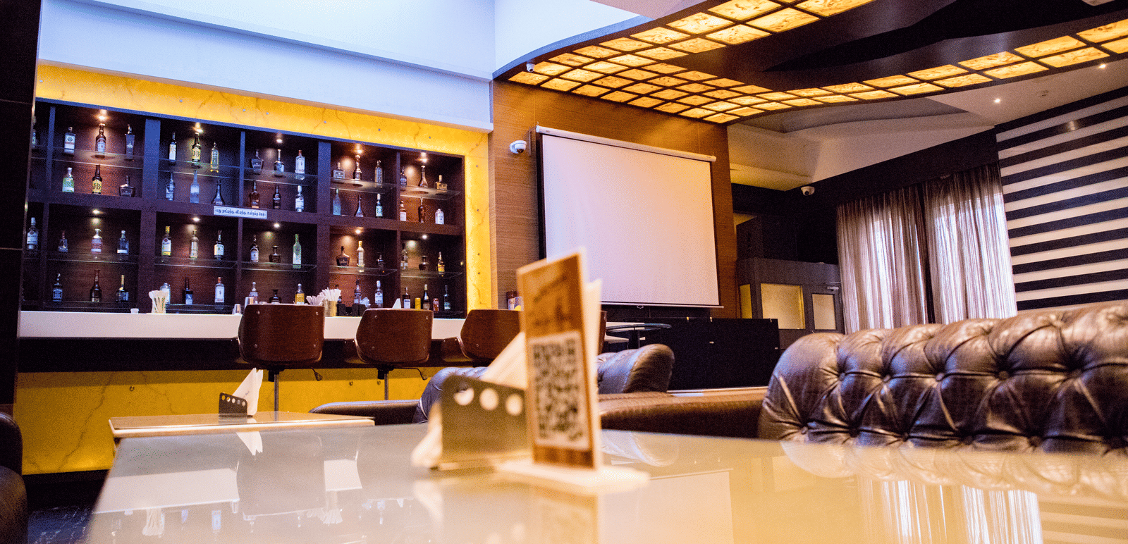 The bar at the Benzz Park, Vellore, taken from the dining table in the restaurant showcasing various liquor bottles on display behind the bar counter.