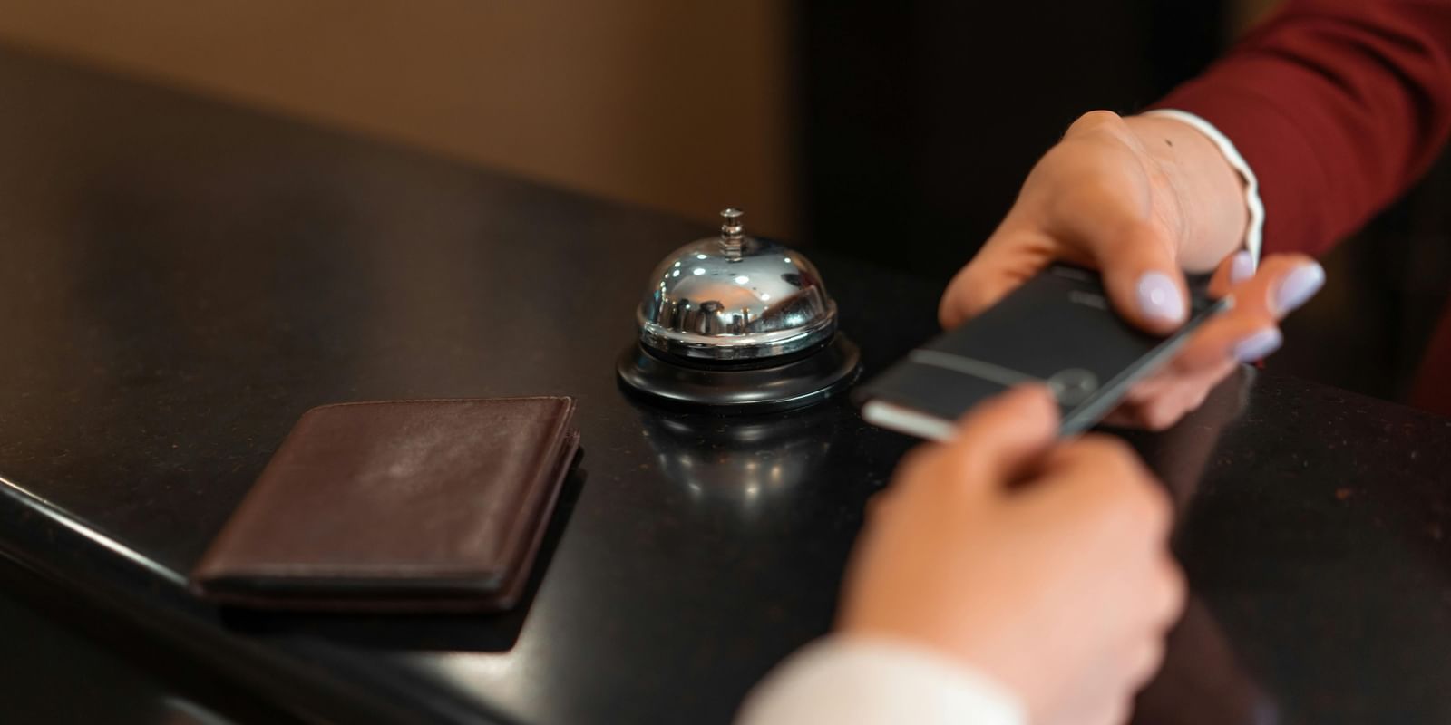 A hand giving and another hand holding onto a small note over the reception desk, with a bell to the side.