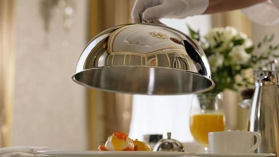 a butler wearing a white glove lifting a cloche inside a hotel room