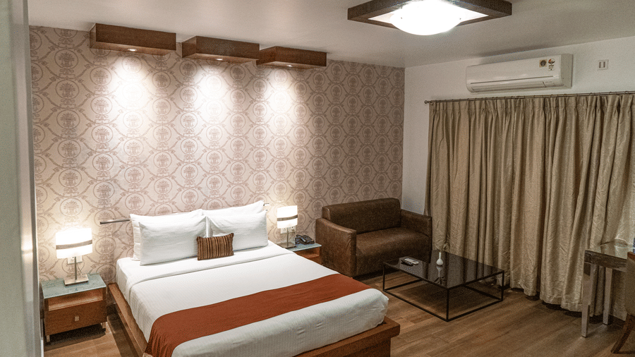 An elevated view of the Junior Suite at Sarovar Portico, Bhubaneswar, with the plush king size bed, beside tables, and wooden flooring highlighted under ample overhead lighting.