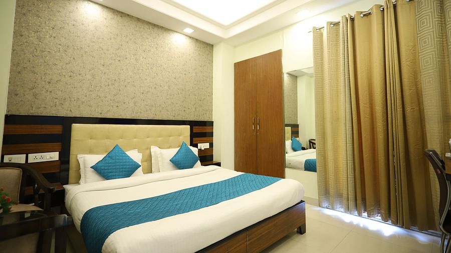 A well-lit room includes a double bed with blue accents, wooden furniture, and a mirror on the wall - Asian Suites Cyber Park, Gurgaon