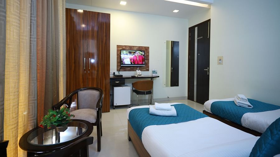A room with two single beds and a seating area, featuring warm lighting and a mirror on the wall - Asian Suites Cyber Park, Gurgaon