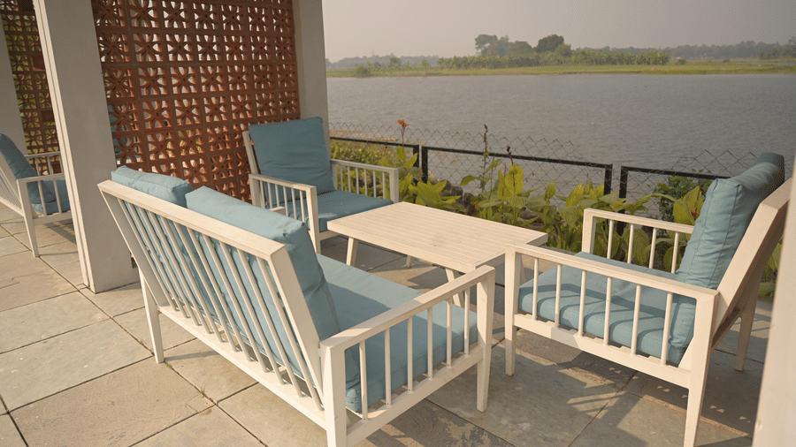 Riverside patio seating with cushioned chairs and a view of the water at Hotel Sonar Bangla, Mayapur.