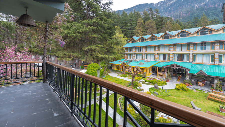 View from a private balcony overlooking the lush green gardens and the main lodge building - Johnson Lodge & Spa, Manali