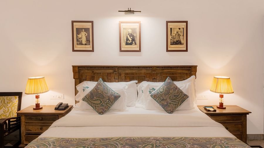 A spacious bed with wooden bedside tables on each side, both featuring lamps, and a photo frame above the headboard at Panna Vilas Palace