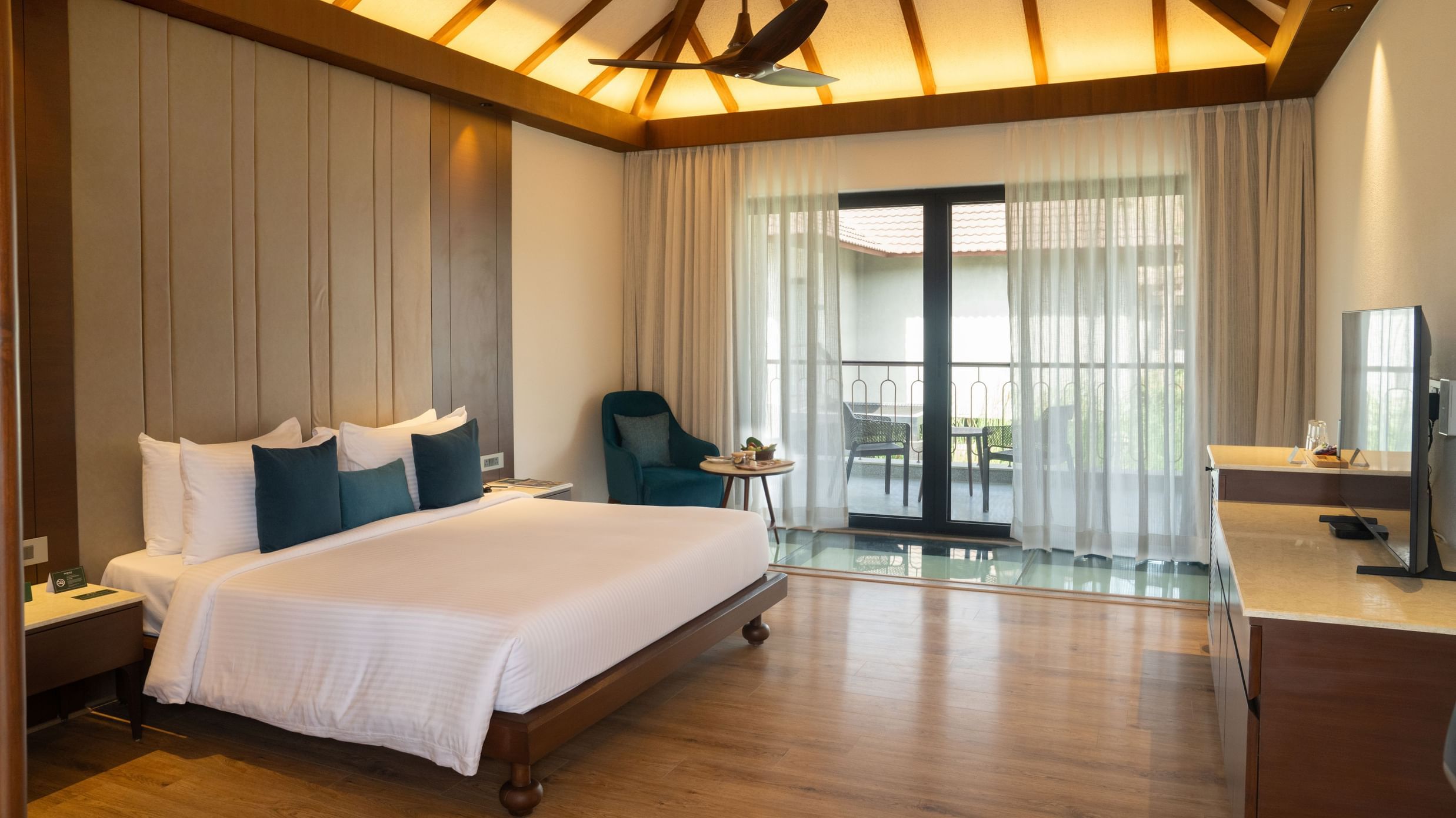 A spacious modern bedroom with a king-size bed, wooden flooring, and a balcony with glass doors at Ananta Spa and Resort, Ajabgarh.