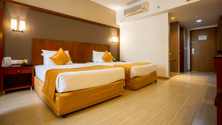 Twin bed room at Featherlite Evoma Hotel with beds dressed in white and gold linen and light wooden flooring throughout the whole room.