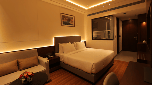 A room at Pride Elite Haridwar featuring king size bed with comfortable sofas. The room is lit with ceiling lights and lights around the bed and sofa.