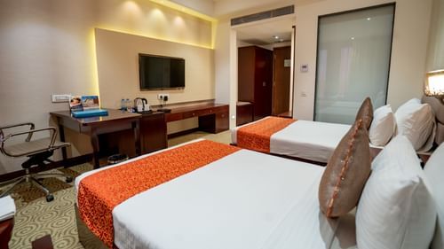 Deluxe Twin at Pride Hotel and Convention Centre, Indore featuring twin beds placed in front of a TV mounted on the wall next to which a work desk is placed facing the wall