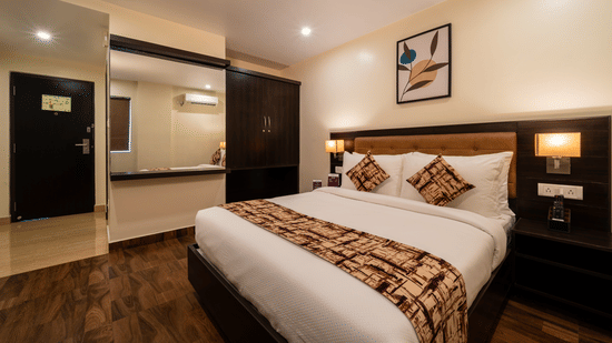 A bedroom interior at VITS Select, Bengaluru, featuring a plush bed, wooden flooring, and a bathroom entrance with mirror.