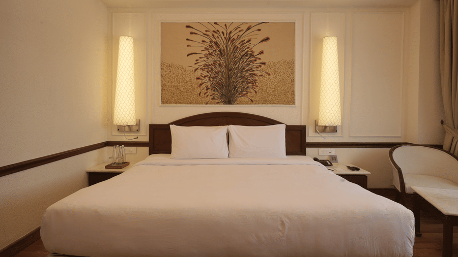 A double bed with a decorative wall panel and vertical light fixtures sits center stage in the Superior King room at Clarks Amer, Jaipur.