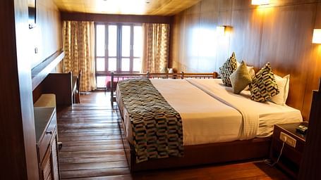 A side view of the green accented double bed facing the TV in the warmly lit Double room at the Cedar Inn in Darjeeling.