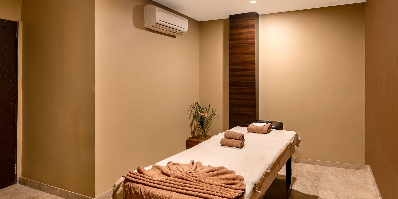 A massage room with a table, towels, and a small flower arrangement - Via Lakhela Resort & Spa, Kumbhalgarh