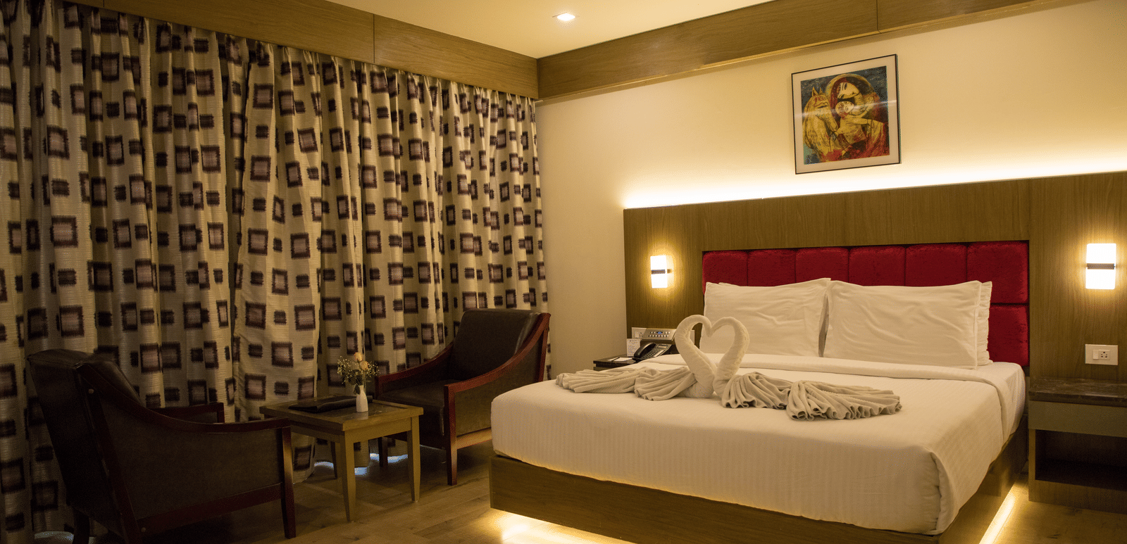 Full view of the Deluxe Room at the Benzz Park, Vellore, featuring a double bed with under-bed lights alongside a common seating area.