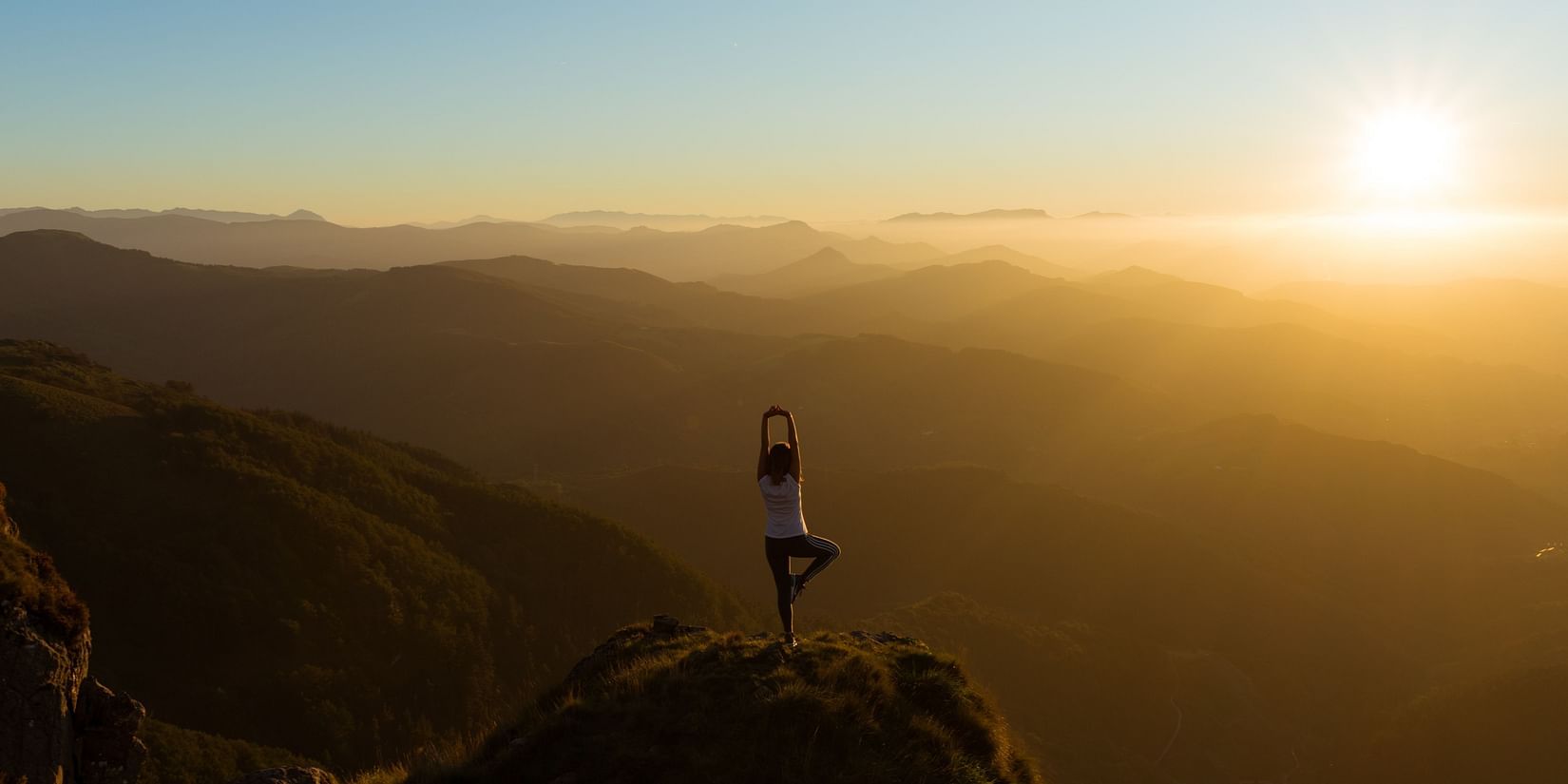 a person practicing yoga on hilltop during sunrise
