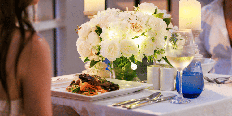 A table set with white flowers, candles, plated food, and wine at The Soco House, with two diners partially visible.