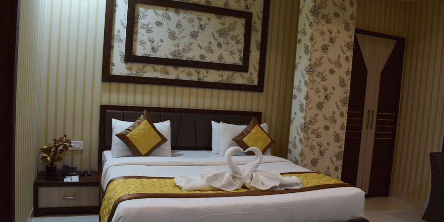 A spacious room with a bed decorated with towel swans and a wooden bedside table at Hotel Uday Palace.