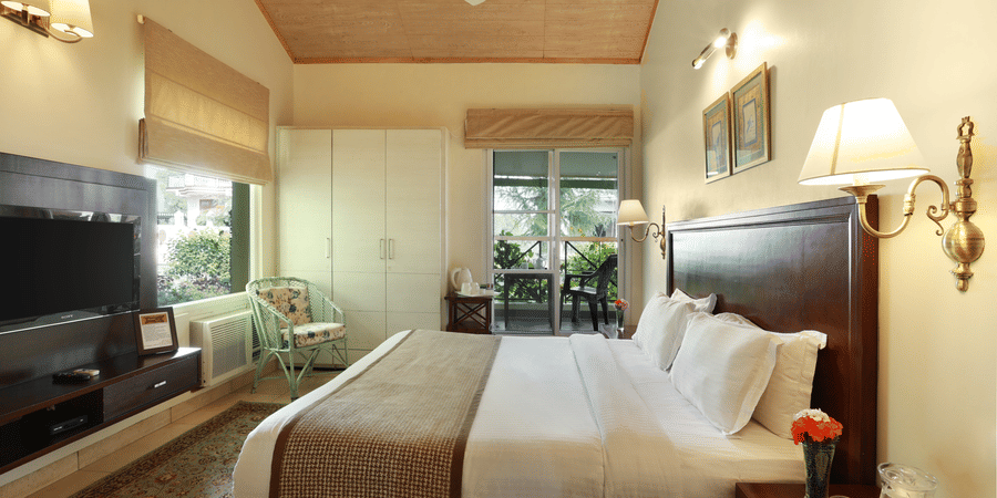 A grand room with a cosy setting showcasing windows with serene view and amenities like bedside lamps, a television, a wardrobe, etc. - Lamrin Norwood Green, Palampur