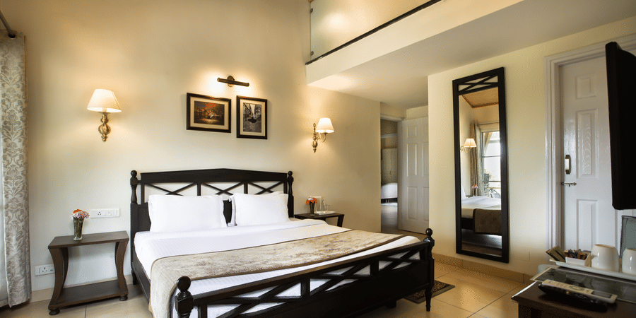 A luxurious room with a king size premium bed with soothing white coloured walls and a wall mirror on the right - Lamrin Norwood Green, Palampur