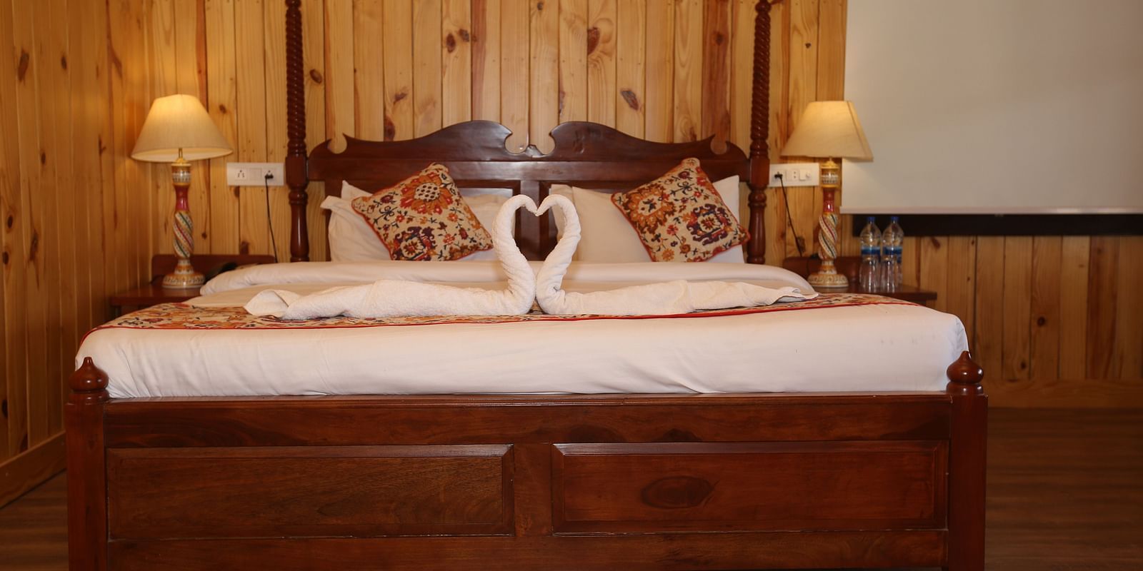 Front view of the king-sized bed, with bedside bedlights and decorative towels on it at Aanandam Resort & Spa