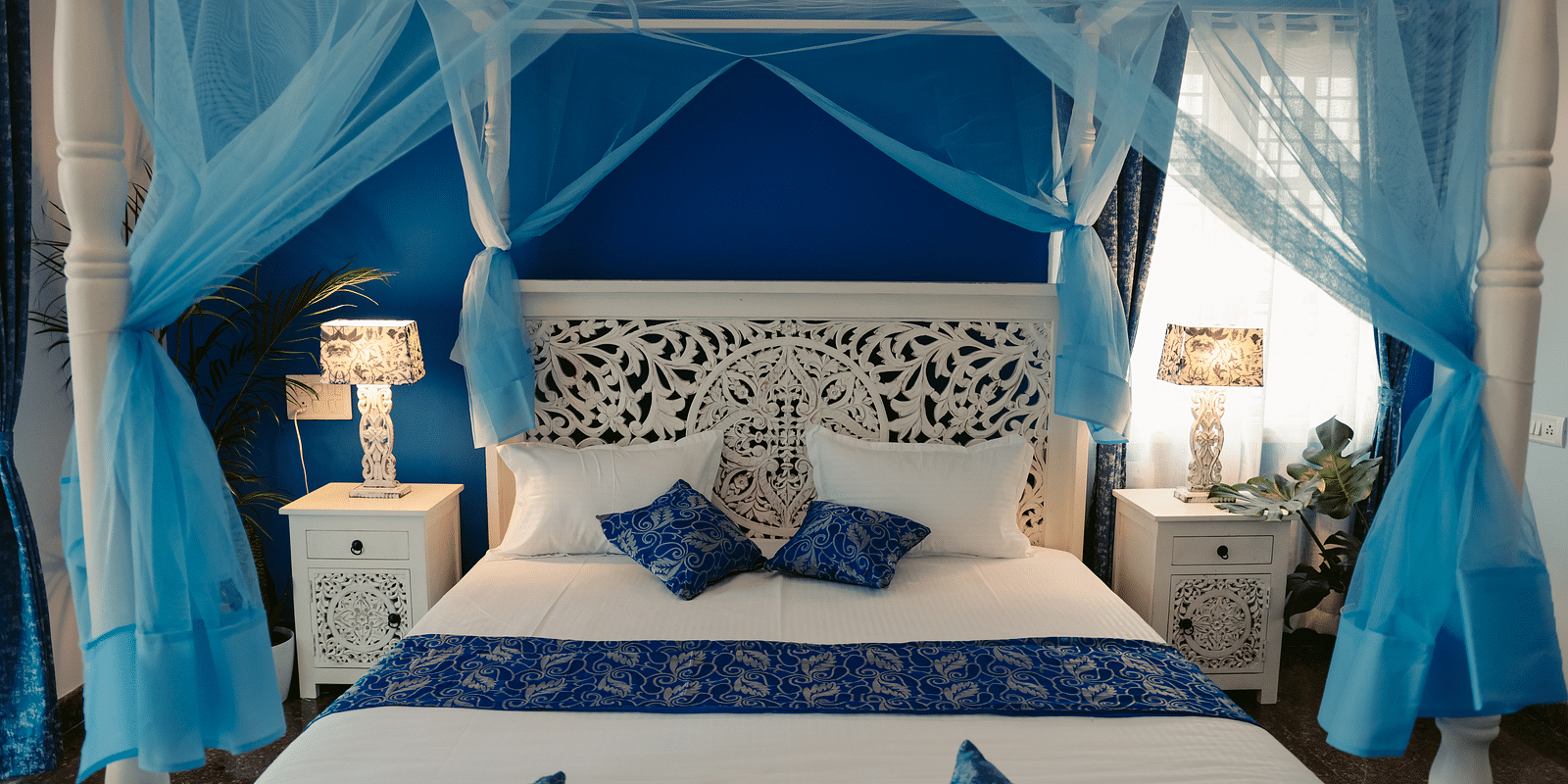 A bedroom with a white four-poster bed draped in sheer blue fabric | Adhyaya Heritage Reverbed