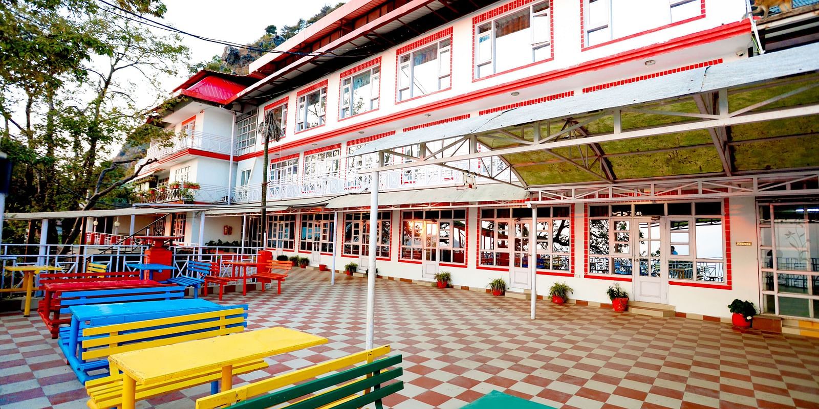 Facade of Amara Hill Queen, Mussoorie with a seating area in front with benches and chairs.