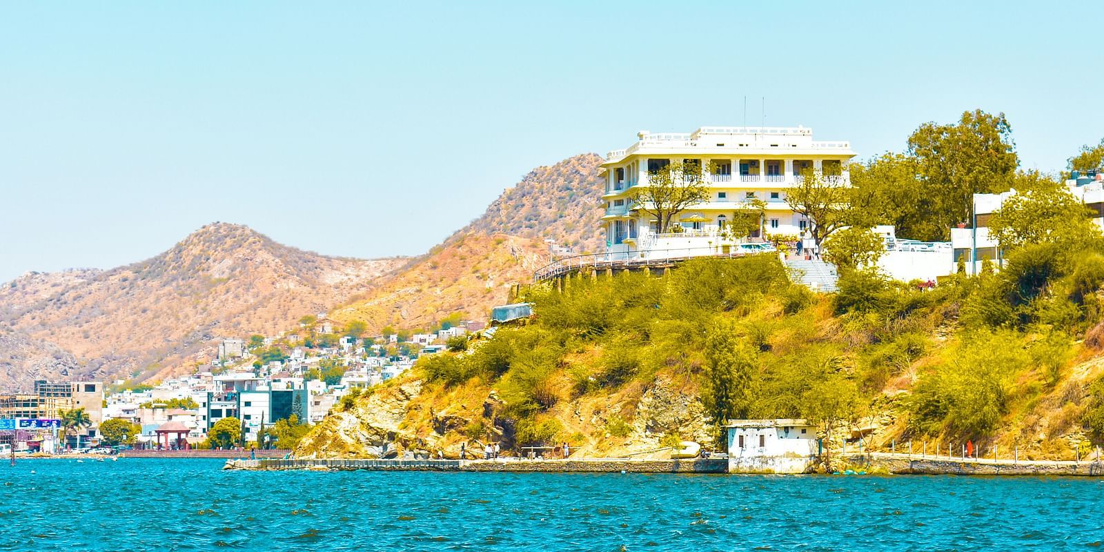 A scenic view of a bright blue lake with a building nestled on a hillside in the background.