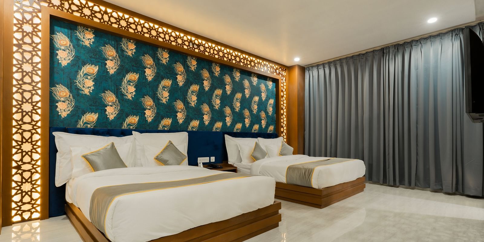 A bedroom at the Bamboo Saa Mulberry Resort featuring two twin beds with white linens and gray throws. A decorative wall panel with a blue and gold pattern is above the beds.