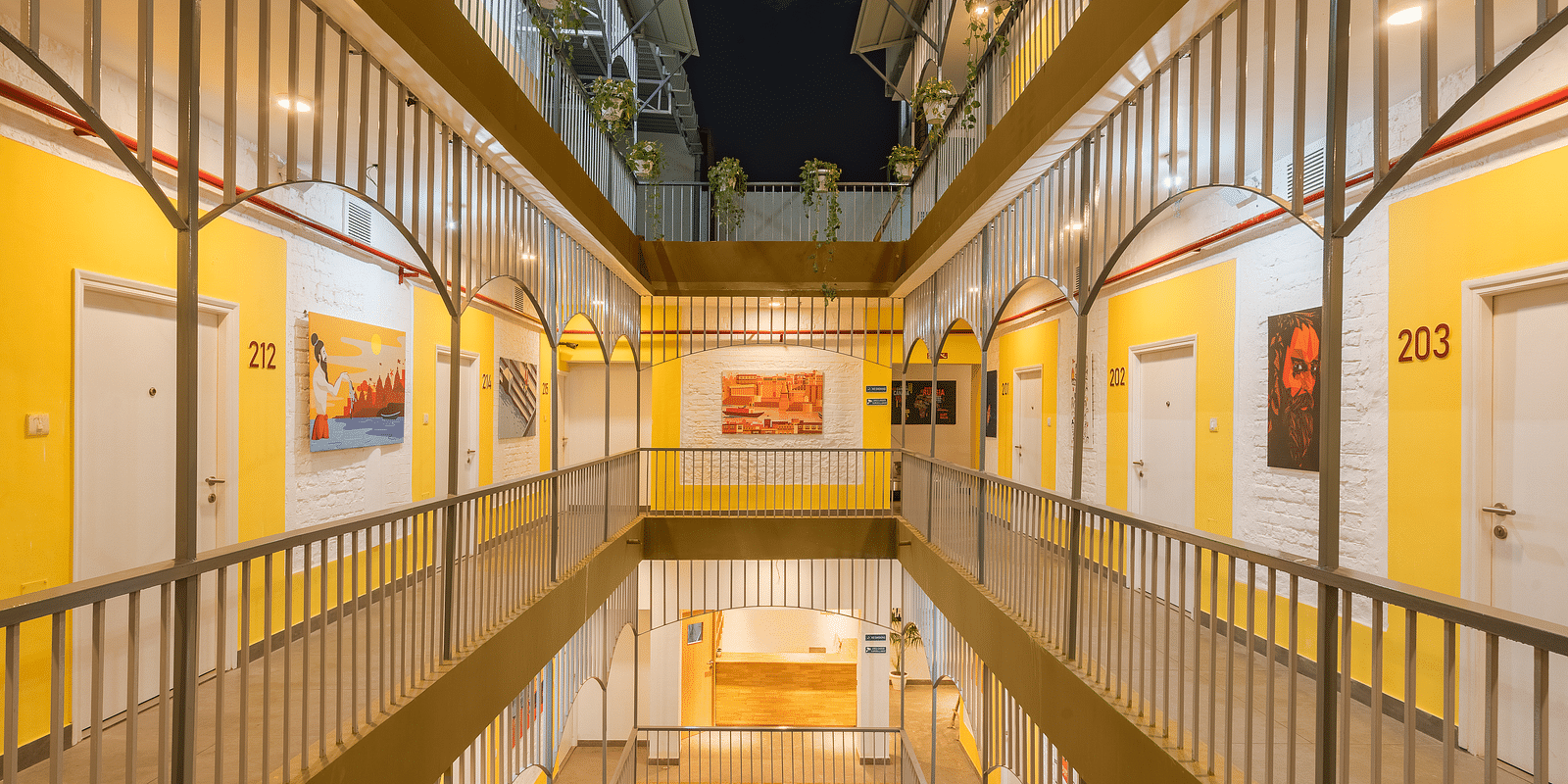 An image of the corridor at Bedzzz Varanasi, brightly lit, with a few wall paintings hanging on the walls, captured in the night.
