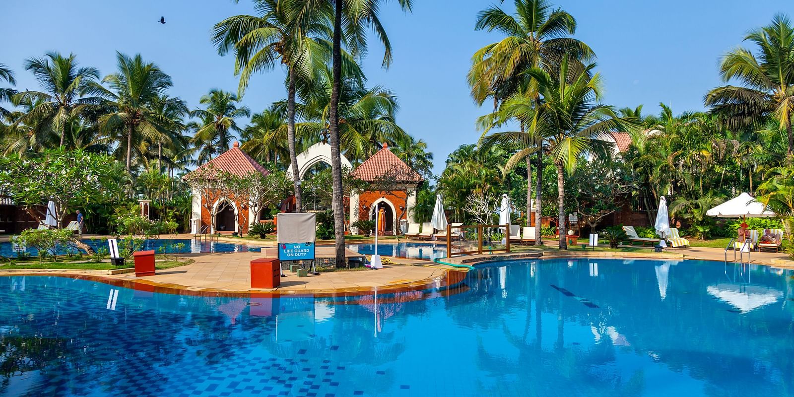 overview of the swimming pool with trees in the background - Caravela Beach Resort Goa