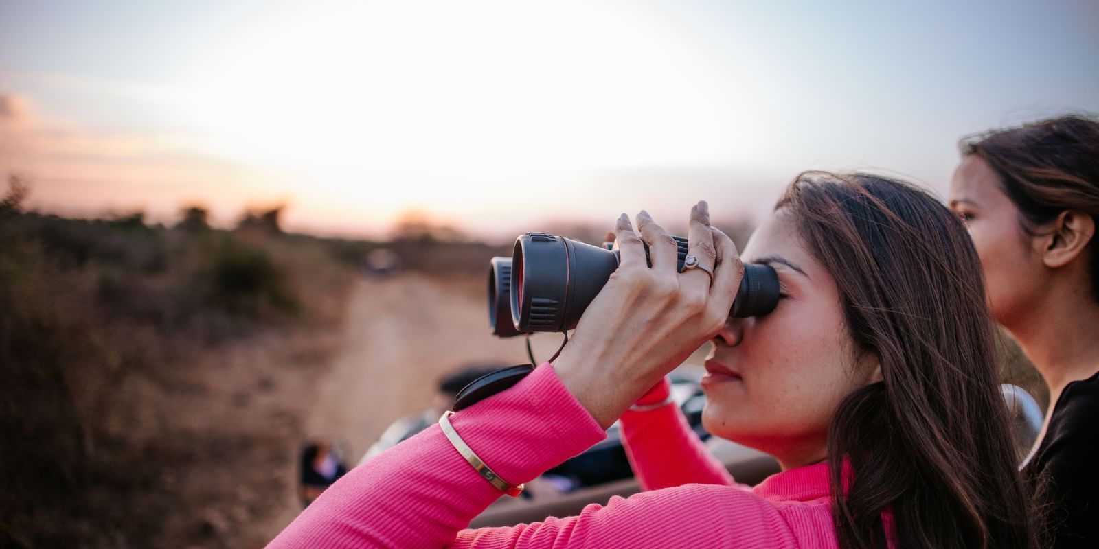 Focus shot of a woman looking through a binoculars and another woman standing beside on the jungle safari trail of Daksh Eden Greenz, Sasan Gir.