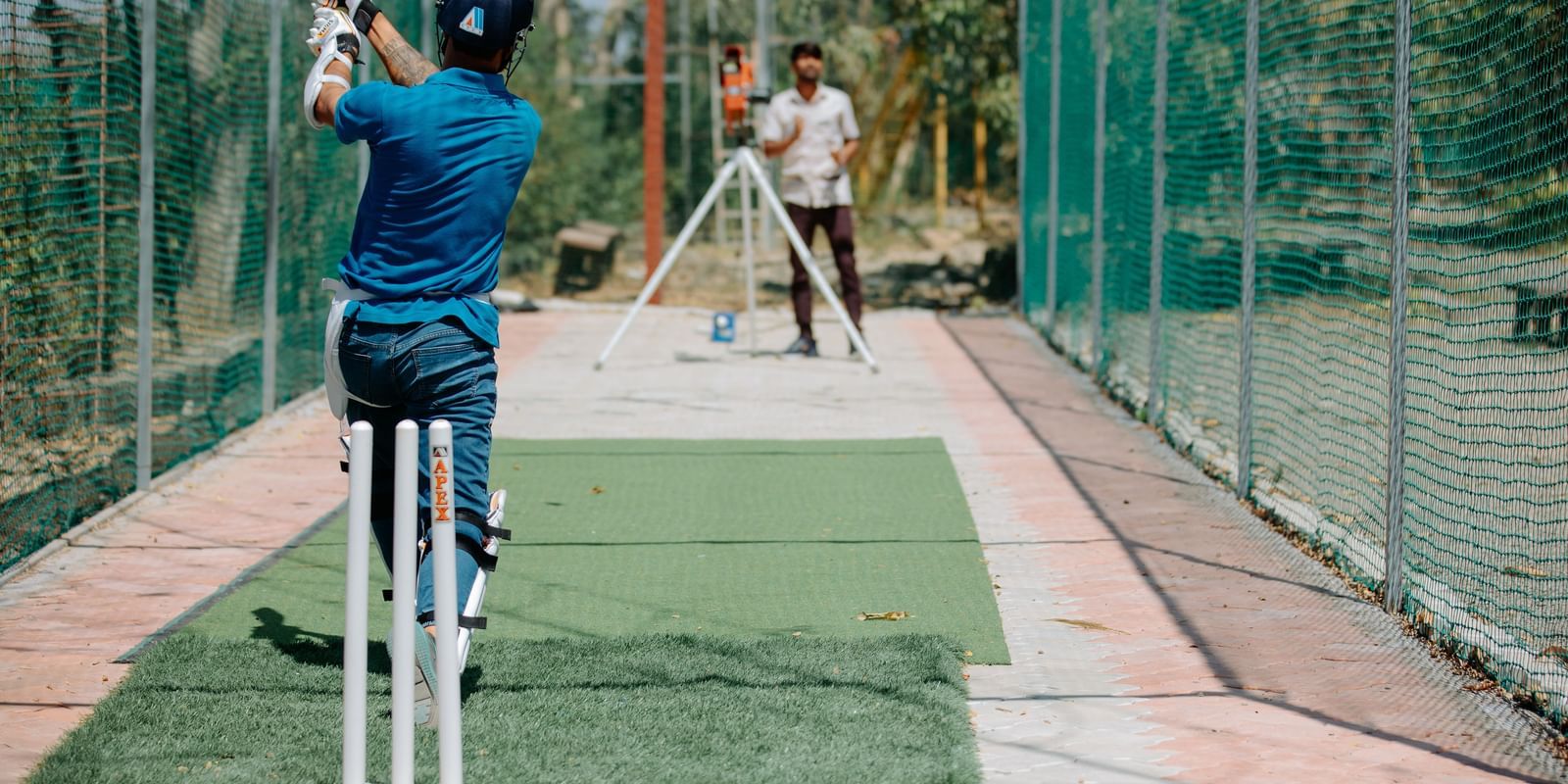 A person playing cricket with a bat in a netted pitch at Daksh Resort & Amusement Park.