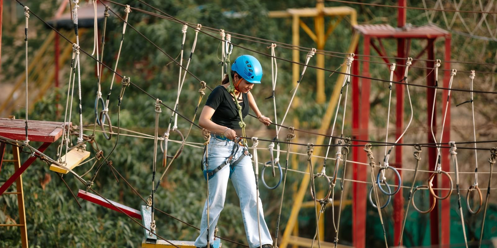 A child navigating a rope obstacle course wearing safety gear at Daksh Resort & Amusement Park.