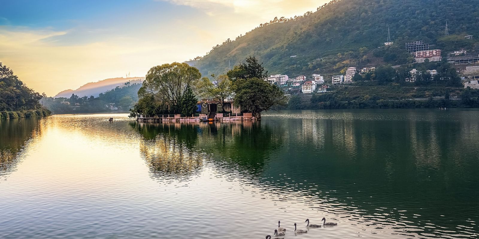 A wide-angle view of Bhimtal Lake with a serene mountain backdrop and ducks peacefully swimming in the calm waters.