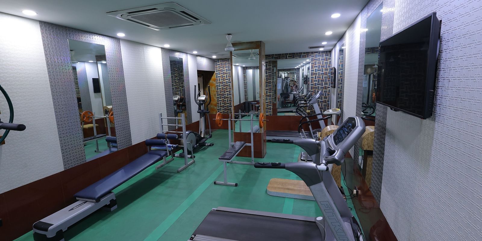 Side view image of a gym at Hotel Amar with gym equipment and a mirror 