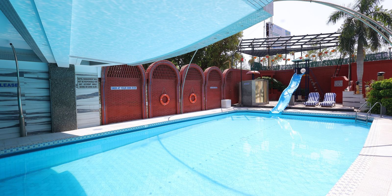 Image of a swimming  pool  of Hotel Amar with a slide and surrounded by plants 