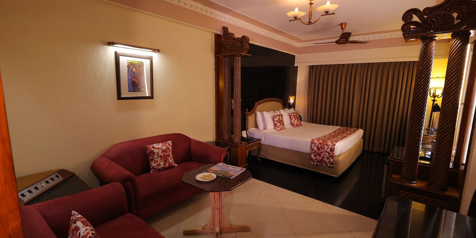 Overview image of Premium room at Hotel Amar with a bed, red sofa, table and long curtains.