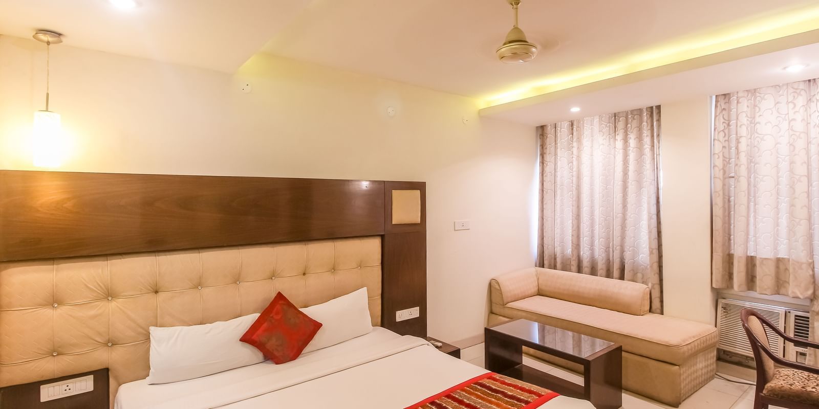 A cosy hotel room with a plush bed, a small sofa, and a glass-topped table. - Hotel Diamond Plaza, Chandigarh.