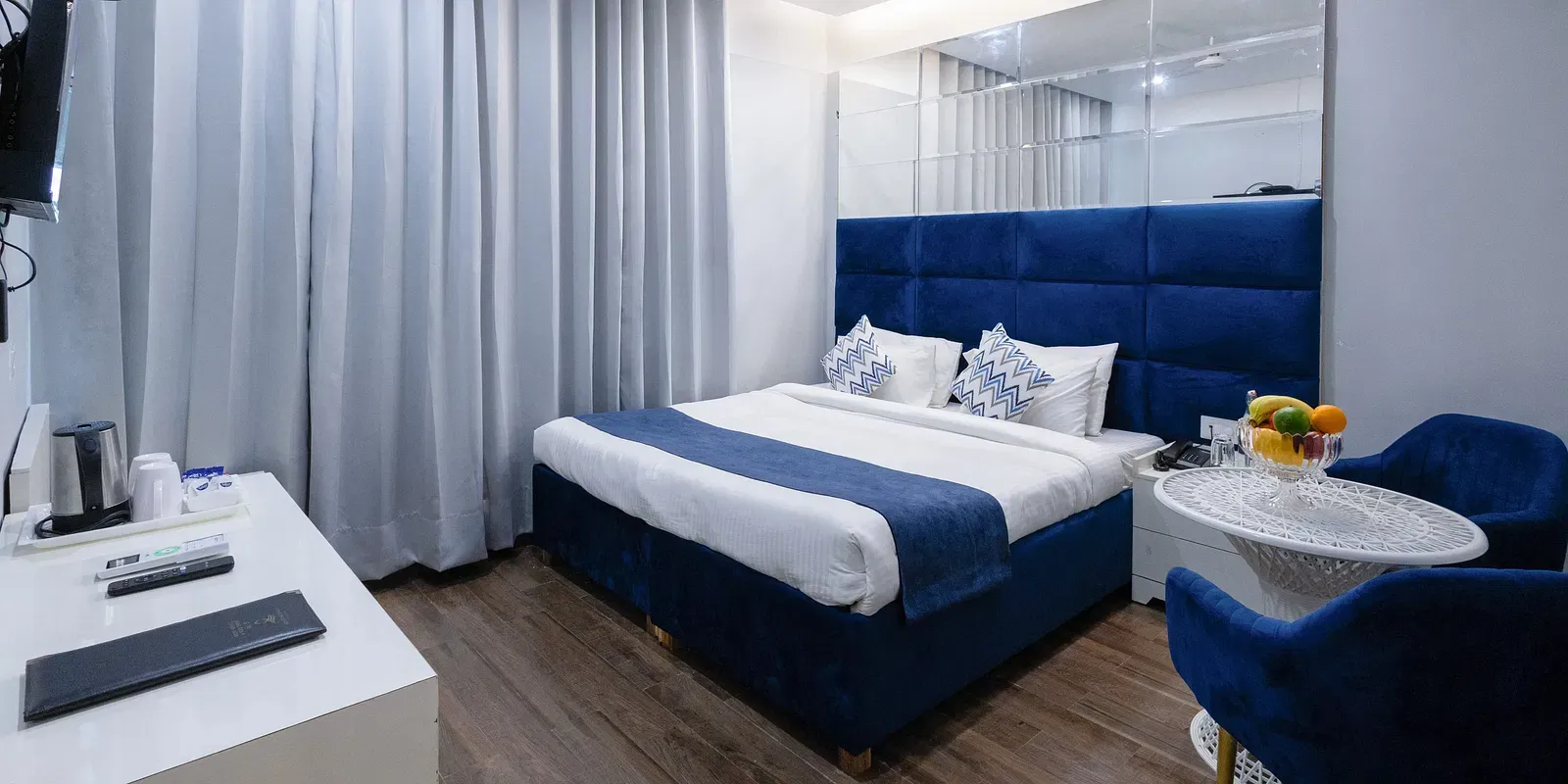 Deluxe Room featuring a king size bed with a blue headboard and white and blue linens, two blue chairs with a small round table, and light wood-look flooring. - Hotel Downtown17, Chandigarh