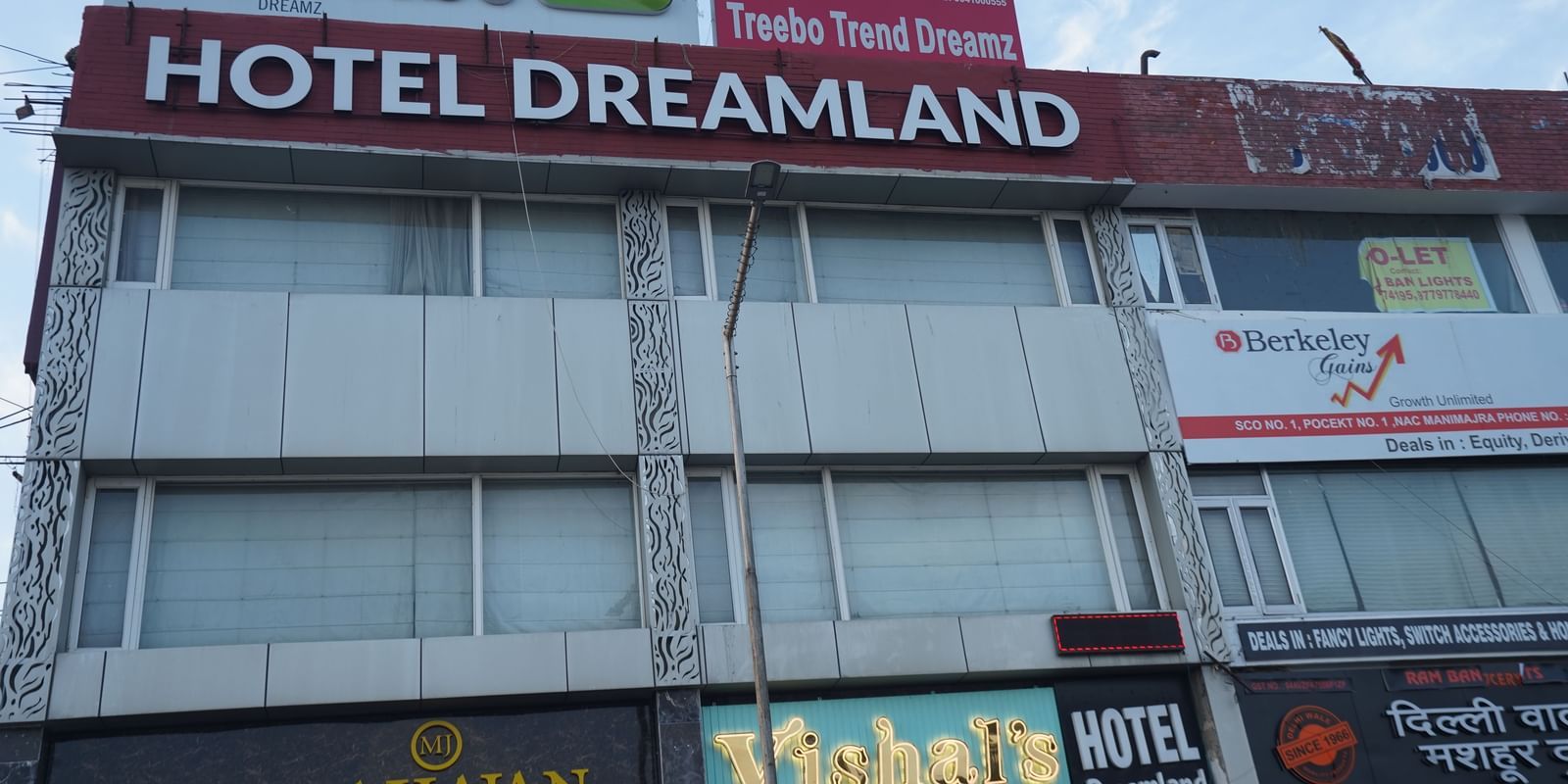 Exterior of the two-storey Hotel Dreamland, Chandigarh with curtains pulled down against glass windows, a street light in the front and patterned steel designs. 